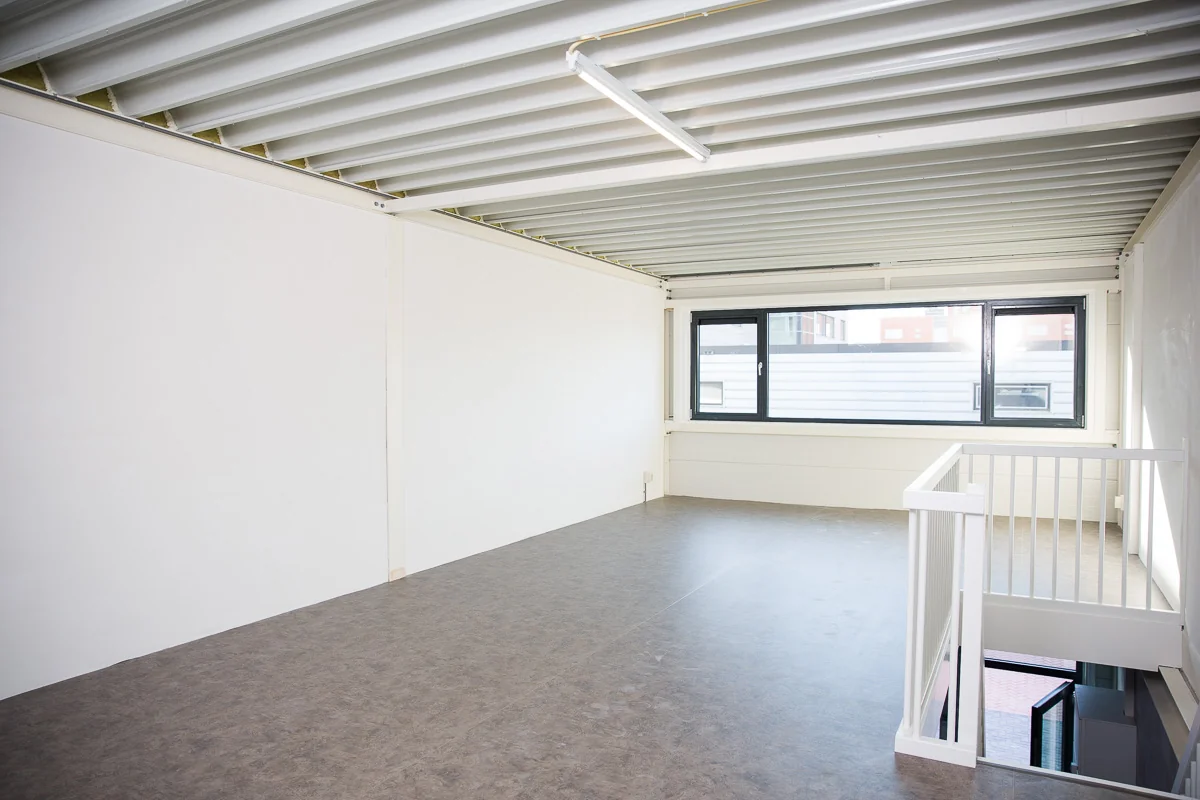 Leeg en modern kantoor- of bedrijfsruimte aan de Laan van 's-Gravenmade met grote ramen en zicht op trap naar beneden.